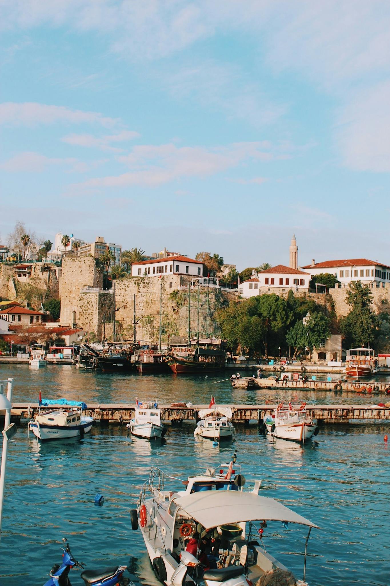 Charming day view of Antalya's historic old harbor with moored boats against ancient stone walls.