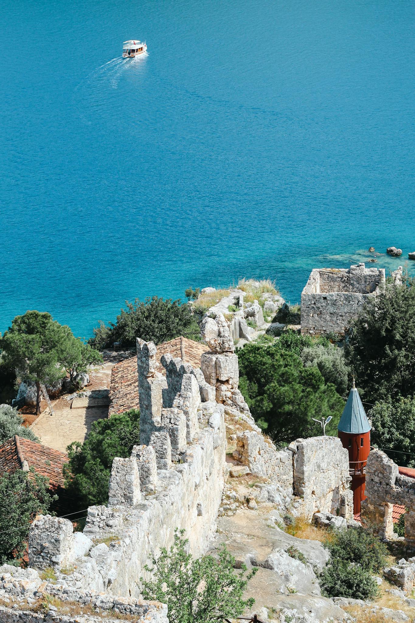 Ruins of an ancient fortress in Antalya, Türkiye, by the blue sea with a lone boat on the horizon.